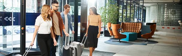 Colegas multiculturales en ropa casual se paran en el vestíbulo de un hotel con su equipaje, listos para un viaje corporativo. - Foto, Imagen