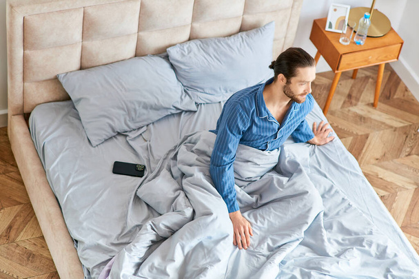 Un uomo con una camicia blu su un letto durante una mattinata tranquilla. - Foto, immagini
