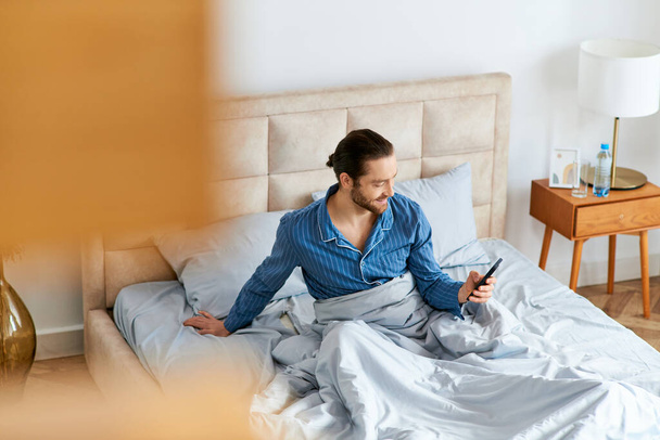 Ein Mann sitzt auf seinem Bett, in seinen Handybildschirm vertieft. - Foto, Bild