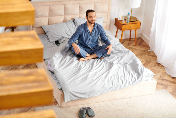 Jóképű férfi békésen gyakorolja a reggeli jógát az ágyán.. - Fotó, kép