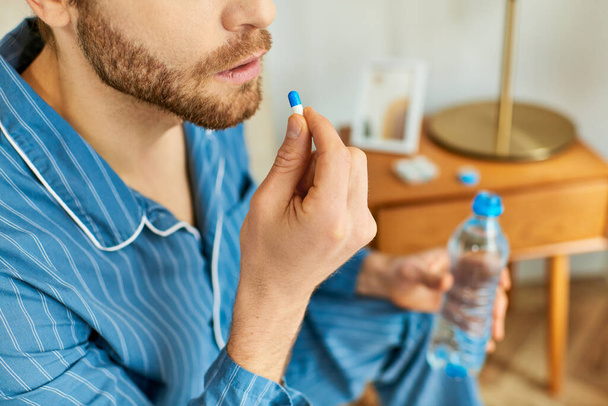Handsome man in a blue shirt holding a bottle of water and pill. - Photo, Image