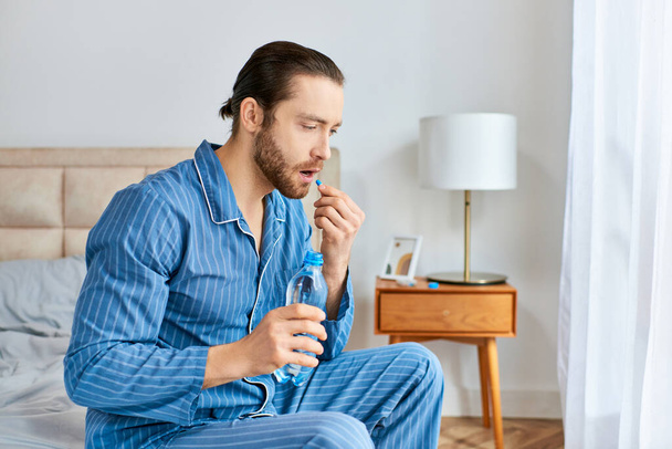 Ένας άντρας κάθεται ήσυχα σε ένα κρεβάτι κρατώντας ένα μπουκάλι νερό και χάπι.. - Φωτογραφία, εικόνα