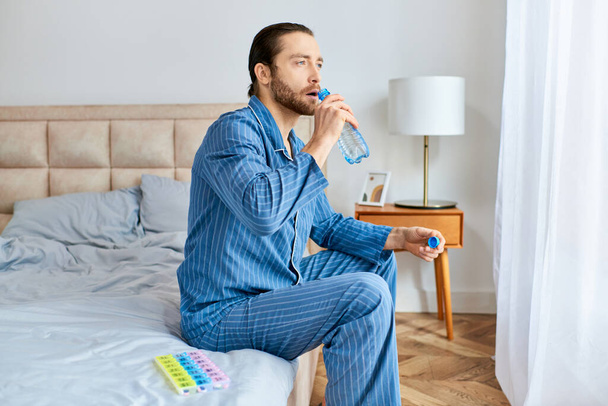 A man sitting on a bed, hydrating with water from a bottle. - Photo, Image