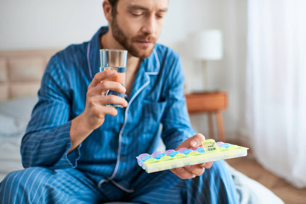 Um homem relaxando em uma cama, segurando pílulas, desfrutando de sua manhã. - Foto, Imagem