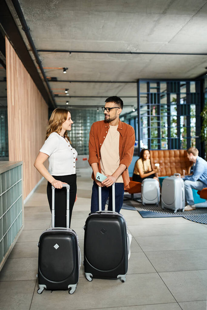 Un hombre y una mujer de pie juntos, equipaje en la mano, en el vestíbulo de un hotel durante un viaje corporativo. - Foto, imagen