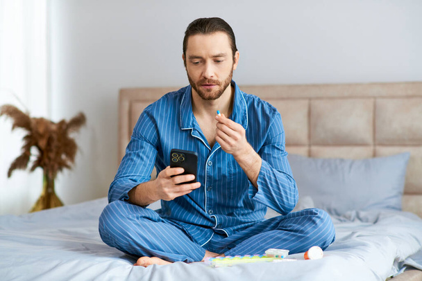 Mann sitzt auf Bett, konzentriert auf Handy-Bildschirm, Morgenlicht erhellt Raum. - Foto, Bild