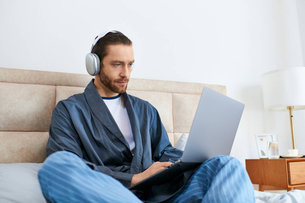 Мужчина медитирует на кровати, просматривает интернет на ноутбуке. - Фото, изображение