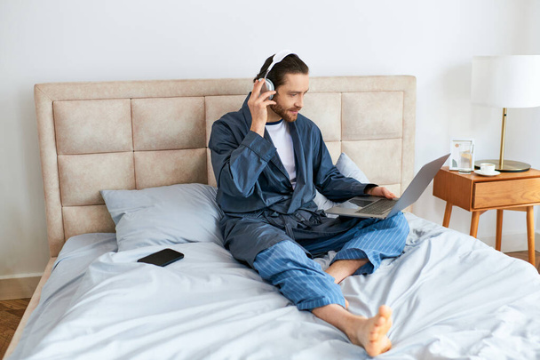 Ελκυστικός άντρας στο κρεβάτι, με ακουστικά και laptop. - Φωτογραφία, εικόνα