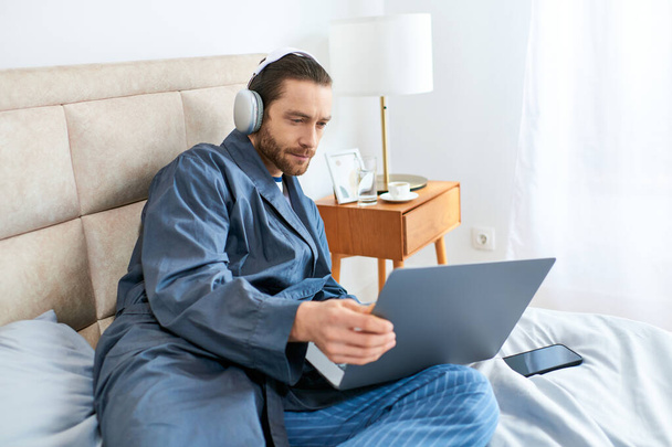 Человек сидит на кровати, сосредоточен на экране ноутбука. - Фото, изображение