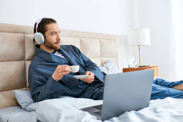 Un uomo si rilassa su un letto con un computer portatile e cuffie, incarnando pace e concentrazione. - Foto, immagini