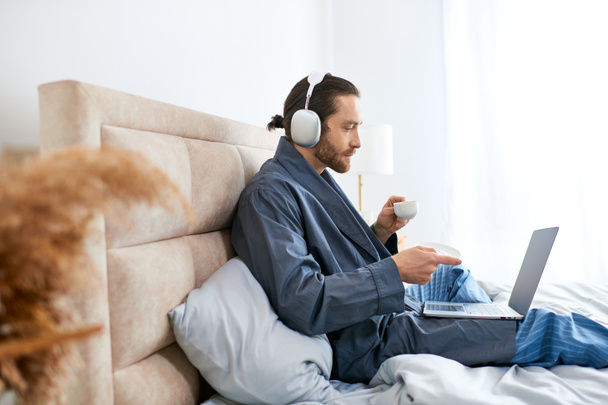 Um homem na cama com laptop e fones de ouvido imersos em sua rotina matinal. - Foto, Imagem