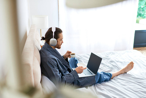 Hombre sentado en la cama, utilizando el ordenador portátil para la relajación de la mañana. - Foto, imagen