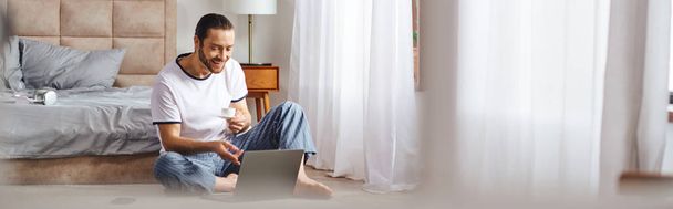 Un hombre absorto en el uso de un ordenador portátil mientras está sentado en el suelo. - Foto, imagen