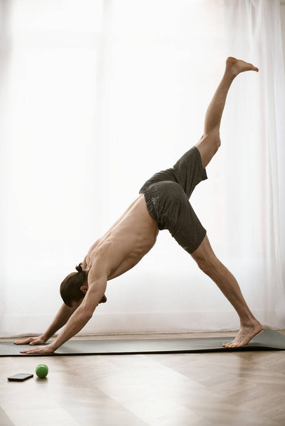 Handsome man in a yoga pose by a window at home. - Photo, Image
