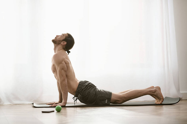 Sesión de yoga en casa por la mañana con un hombre enfocado que practica en una esterilla. - Foto, Imagen