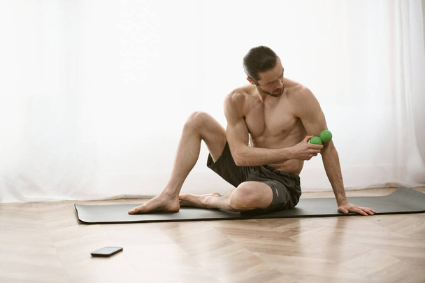 Muž bez košile sedí na podložce a drží zelený masážní míček.. - Fotografie, Obrázek