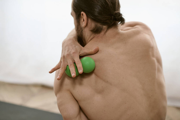 Sağ elinde yeşil masaj topu olan bir adam evde yoga yapıyor.. - Fotoğraf, Görsel