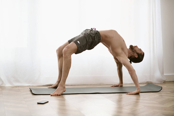 Sesión de yoga en casa como un hombre practica una pose desafiante en su esterilla. - Foto, imagen