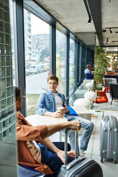 Dos empresarios, sentados con el equipaje, tomando un descanso en una mesa en un hotel durante su viaje corporativo. - Foto, imagen