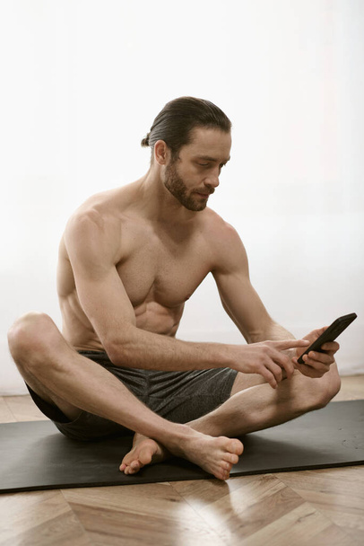 Przystojny mężczyzna, w domu, spokojnie uprawia jogę podczas korzystania z telefonu komórkowego. - Zdjęcie, obraz