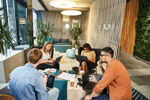 Een divers team van collega 's verdiept in werk, laptops op tafel, samenwerken en brainstormen in een eigentijdse kantooromgeving. - Foto, afbeelding