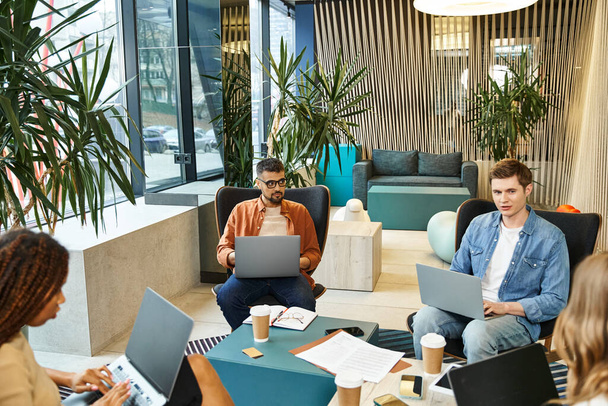 Un groupe diversifié de collègues assis autour d'une table avec des ordinateurs portables, collaborant sur des projets dans un espace de coworking moderne. - Photo, image