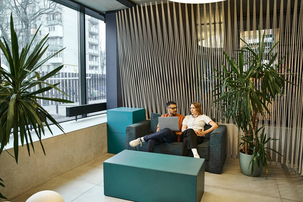 Zwei Profis aus einem Start-up-Team sitzen auf einer trendigen Couch in einem modernen Büroraum und machen eine Pause von der Arbeit. - Foto, Bild