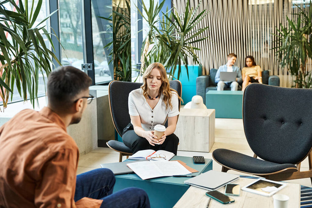 Egy nő ül egy székben a kollégák között egy szobában, megtestesítve a startup csapat szellemét és a modern üzleti életmódot.. - Fotó, kép