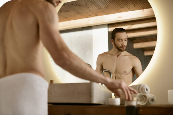 Pohledný muž v bílém spodním prádle stojí před zrcadlem, účastní se péče o pleť rutiny. - Fotografie, Obrázek