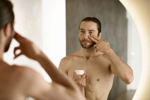 A man applying cream in front of a mirror during his morning routine. - Photo, Image