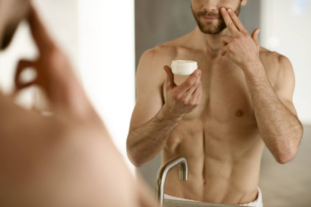 Ένας άντρας να βάζει κρέμα μπροστά στον καθρέφτη κατά τη διάρκεια της πρωινής του ρουτίνας.. - Φωτογραφία, εικόνα