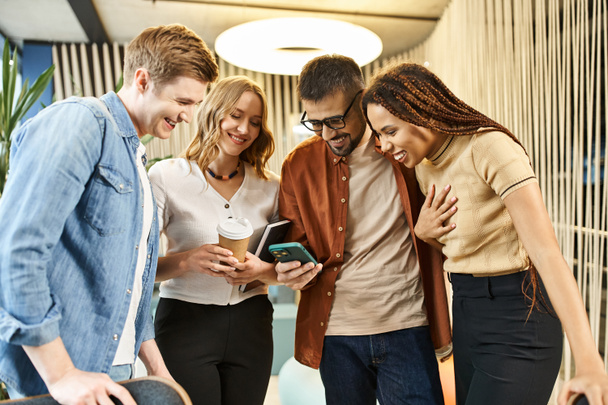 Un grupo de colegas en un espacio de coworking, absortos e interactuando con un teléfono celular, que refleja el estilo de vida empresarial moderno. - Foto, Imagen