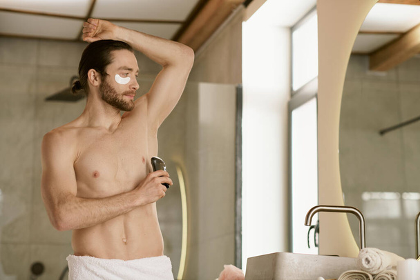 Shirtless man using deodorant in front of mirror, part of daily routine. - Photo, Image