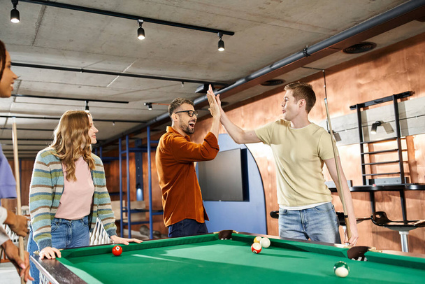 A group of colleagues from a coworking space gather around a pool table, enjoying a break and building team camaraderie. - Photo, Image