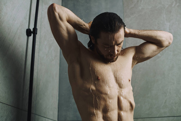 Bez koszuli mężczyzna angażujący się rano stojąc pod prysznicem. - Zdjęcie, obraz
