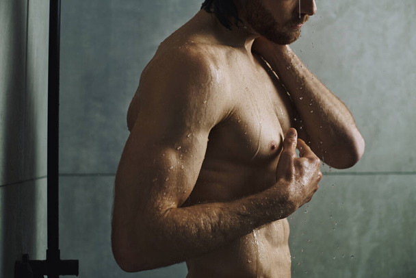 Shirtless man stands before shower, part of his morning skincare routine. - Photo, Image