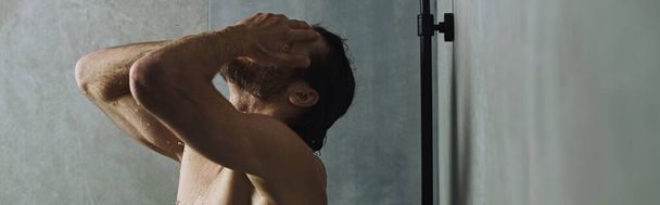 Человек без рубашки принимает душ, заботясь о своей утренней рутине.. - Фото, изображение