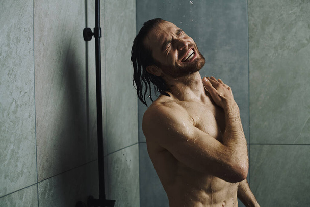 Knappe man, shirtloos, staat klaar om te douchen, gericht op zijn ochtend routine. - Foto, afbeelding