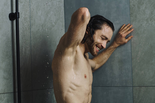 Мужчина без рубашки принимает освежающий душ в домашней ванной. - Фото, изображение