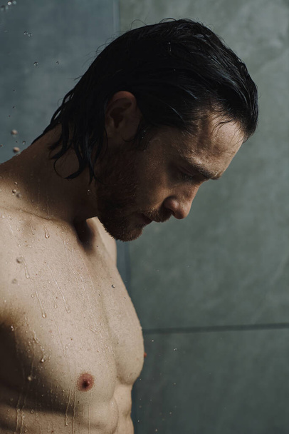 Um homem sem camisa está diante de um chuveiro, se preparando para sua rotina matinal. - Foto, Imagem