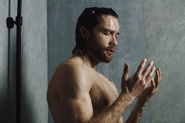 Een man die in een douche staat met zijn handen in de lucht, genietend van zijn ochtendroutine. - Foto, afbeelding