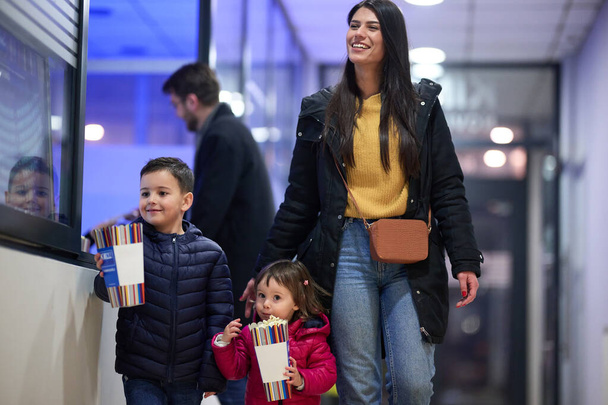 A young couple with their children stands outside the cinema, purchasing freshly popped popcorn before the start of the movie and entry into the theater. - Photo, image