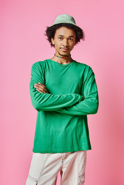 Een vrolijke jonge Afro-Amerikaanse man met krullend haar in een groen shirt en broek op een roze achtergrond. - Foto, afbeelding