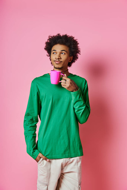 Cheerful African American man in green shirt holds a pink cup against a vibrant pink background. - Photo, Image
