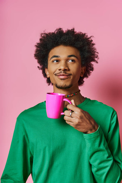 カジュアルなウェアを着た陽気で若いアフリカ系アメリカ人男性が,ピンクの背景に顔の前でカップを持っています.. - 写真・画像