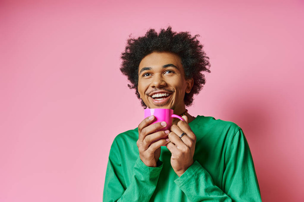 Un allegro giovane uomo afroamericano in abbigliamento casual che tiene una tazza rosa su uno sfondo rosa vibrante. - Foto, immagini