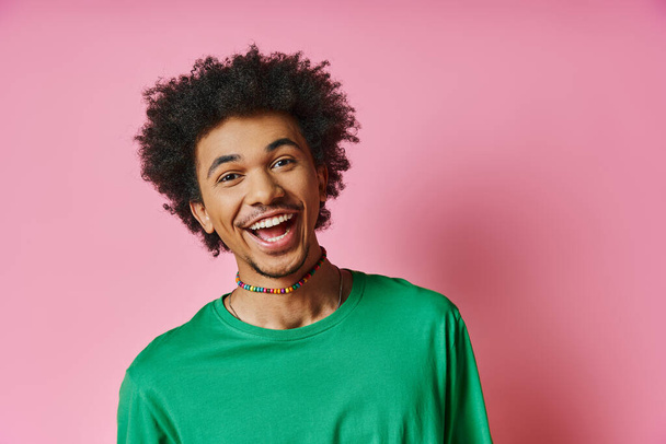 Ein fröhlicher afroamerikanischer Mann mit einem lockigen Afro, der ein grünes Hemd trägt und seine Emotionen auf rosa Hintergrund ausdrückt. - Foto, Bild