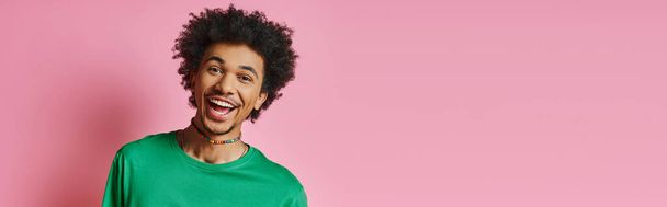 Wesoły młody Afroamerykanin z kręconymi włosami, ubrany w zwykłą zieloną koszulę, uśmiechnięty na różowym tle. - Zdjęcie, obraz