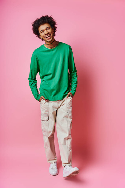 Wesoły młody kręcony Afro-Amerykanin stoi w luźnym ubraniu, pokazując szereg emocji na różowym tle. - Zdjęcie, obraz