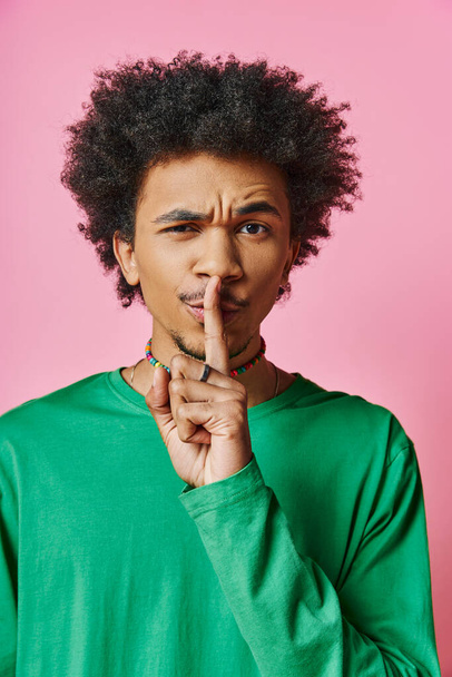 krullend Afro-Amerikaanse man in casual kleding ziet er pensive, met vinger in de mond, tegen roze achtergrond. - Foto, afbeelding